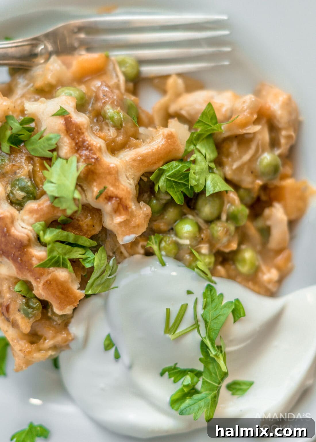 A generous slice of Pumpkin Chicken Pot Pie on a white plate, garnished with fresh parsley and a drizzle of cream