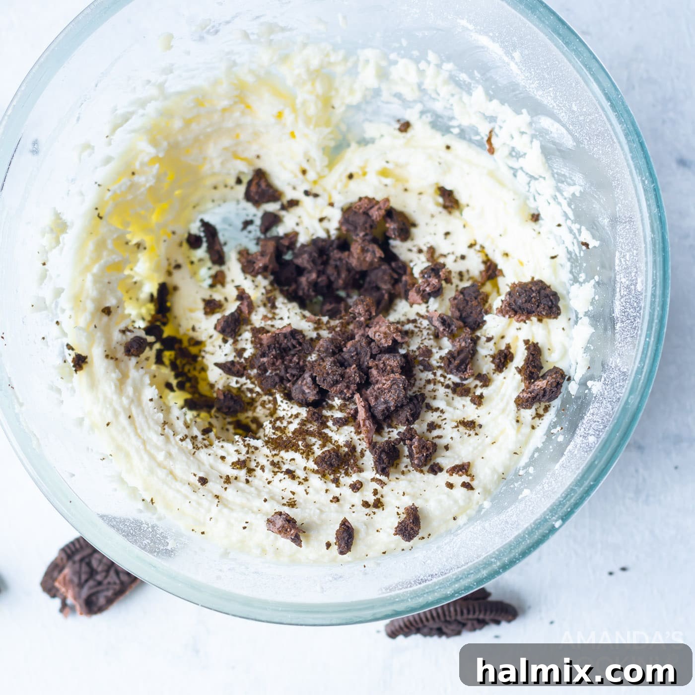 Finely crushed Oreos are being mixed into a bowl of creamy buttercream frosting, creating a delicious cookies and cream topping for cupcakes.