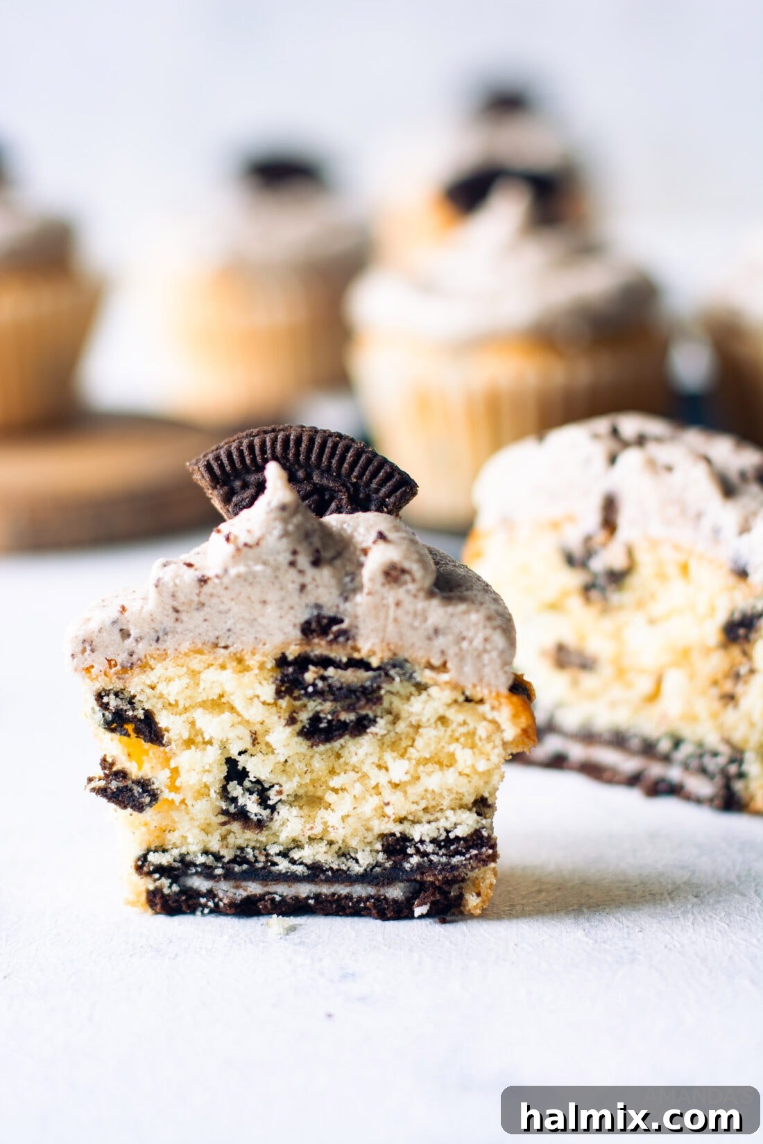 An Oreo Cupcake cut in half, revealing the whole Oreo cookie at the bottom and crushed Oreos mixed into the vanilla cake batter.