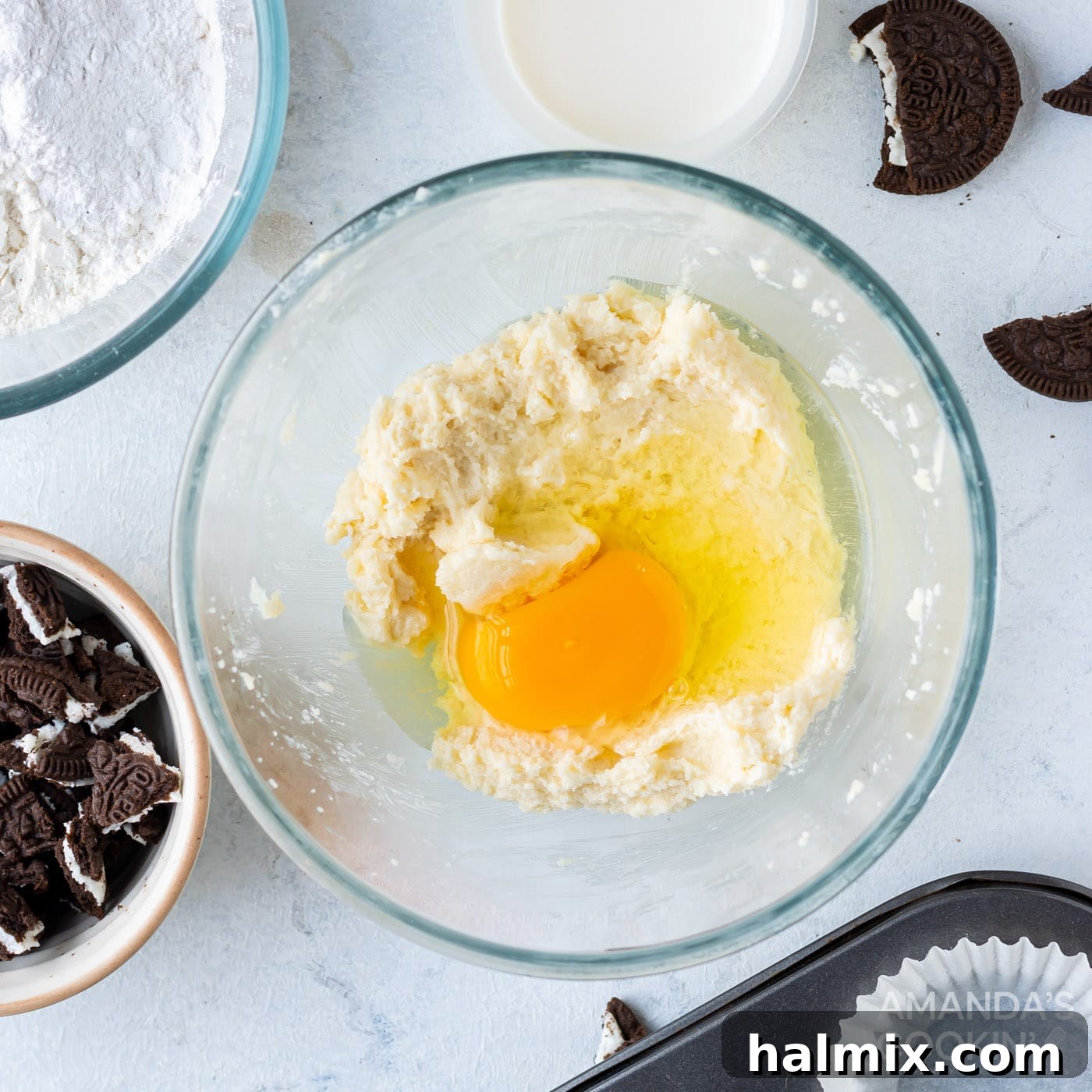 A single egg is being added to the creamed butter and sugar mixture in a bowl, before being mixed into the cupcake batter.