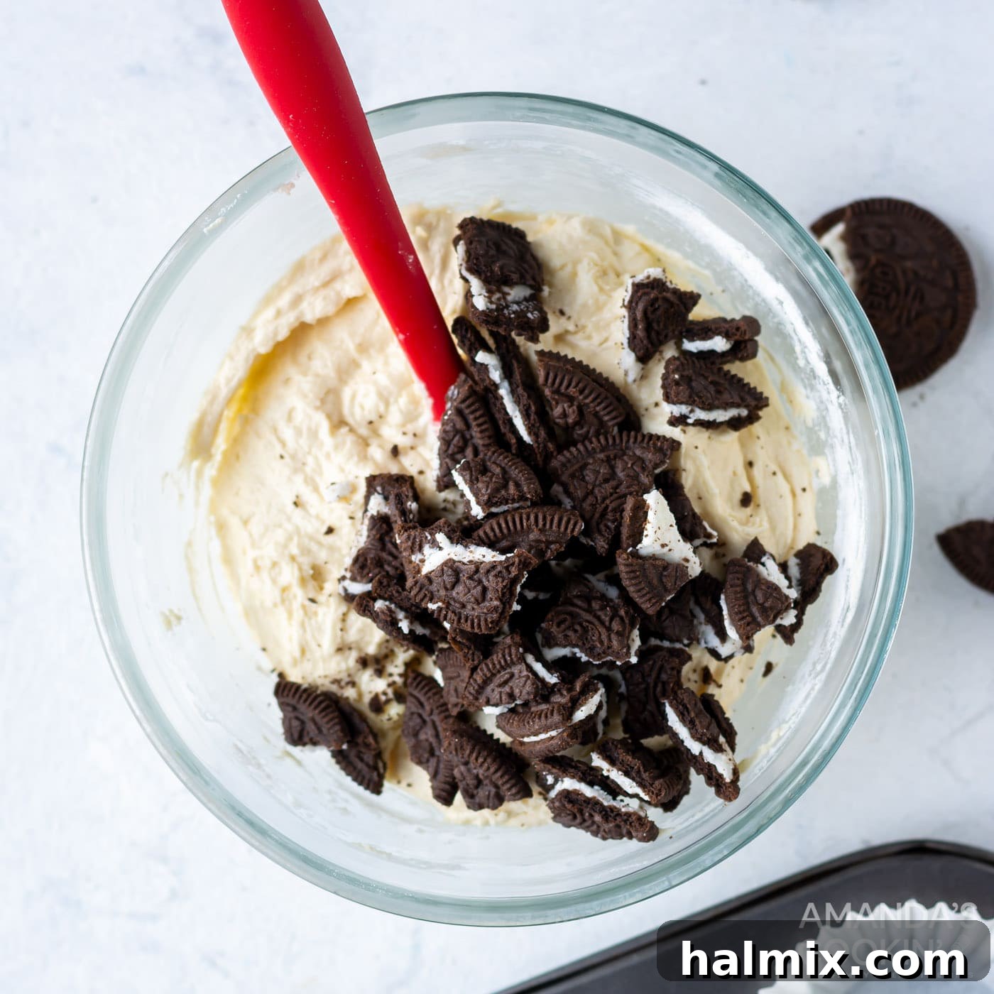 Coarsely crushed Oreo cookies have been added to the vanilla cupcake batter in a mixing bowl, ready to be gently folded in.