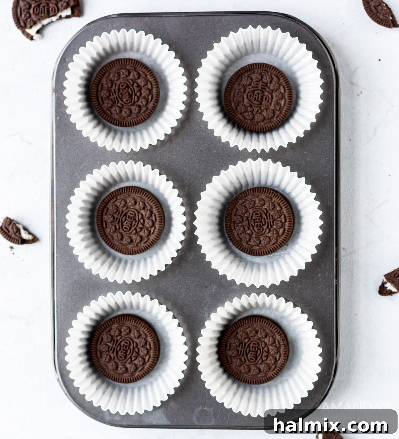 Whole Oreo cookies are carefully placed at the bottom of each paper-lined cavity in a 12-cup cupcake tin.