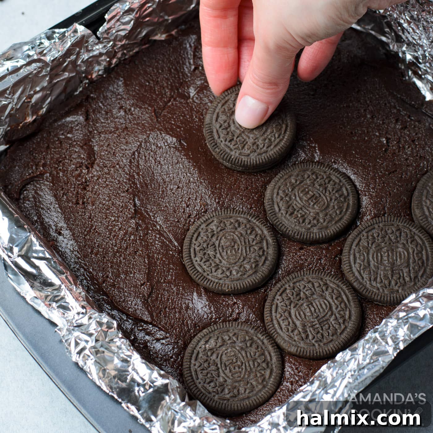 Hand placing whole Oreo cookies on top of brownie batter in a baking pan