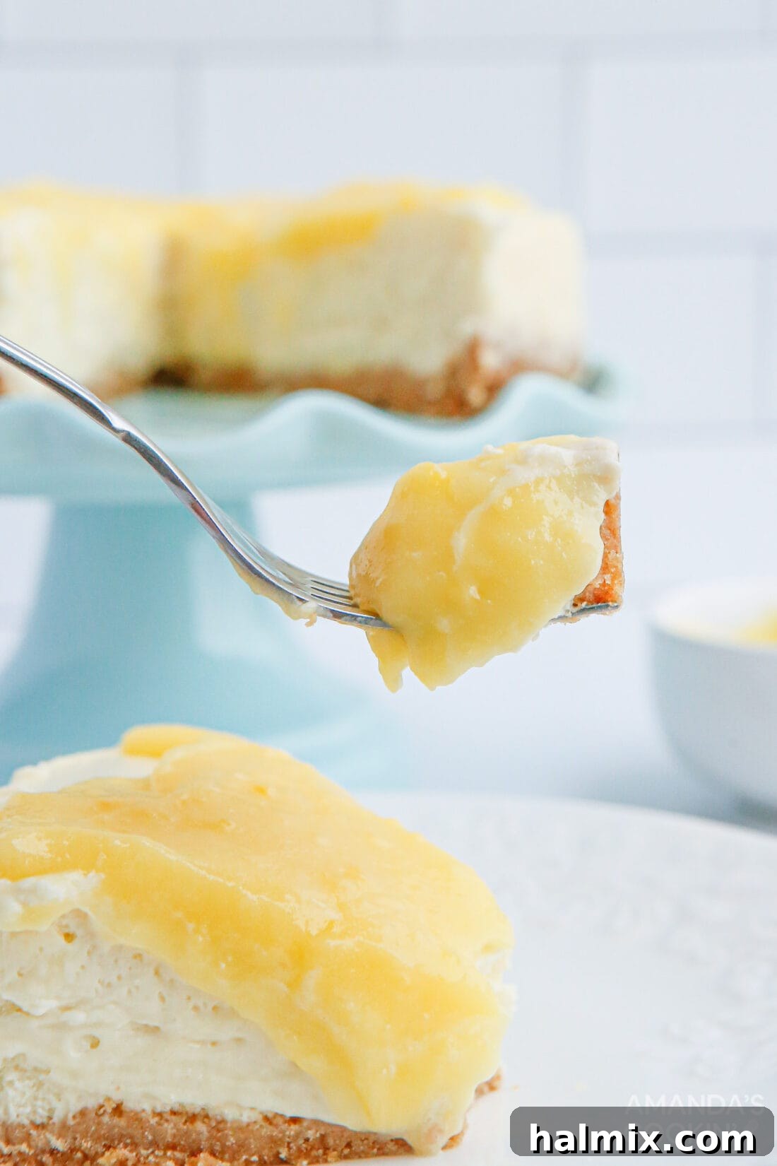 A fork taking a bite from a slice of Instant Pot Lemon Curd Cheesecake, showing its creamy texture and rich lemon curd topping.