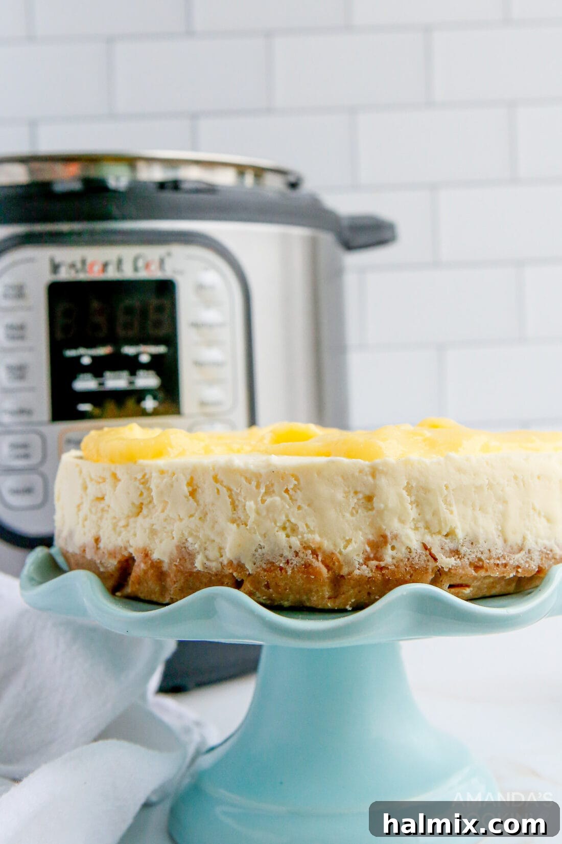 Whole Instant Pot Lemon Curd Cheesecake on an elegant cake plate, showcasing its golden crust and smooth top before the curd is added.