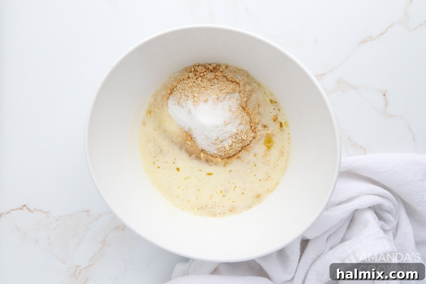 Graham cracker crumbs, melted butter, and sugar are mixed in a bowl, forming the base for the cheesecake crust.