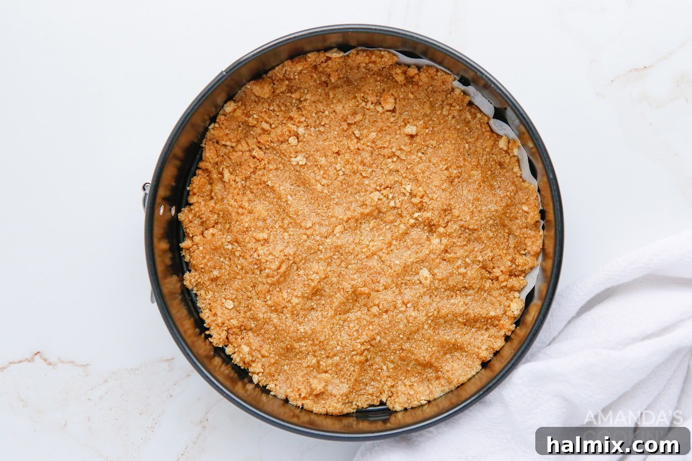 The graham cracker mixture is firmly pressed into the base of a springform pan, creating a solid crust.