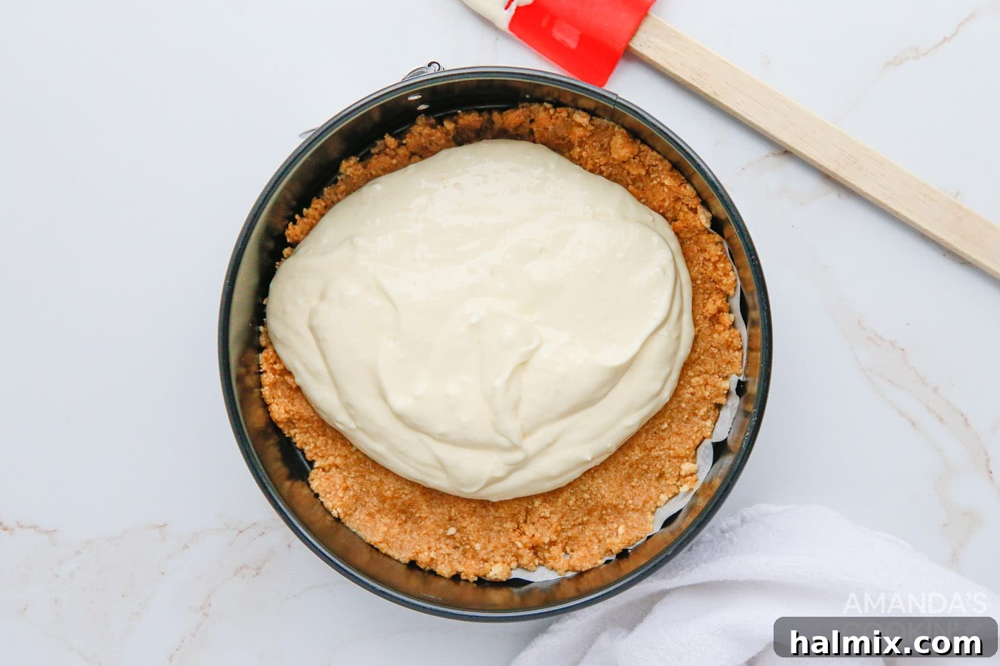 The smooth, creamy cheesecake filling is poured over the prepared graham cracker crust in the springform pan.