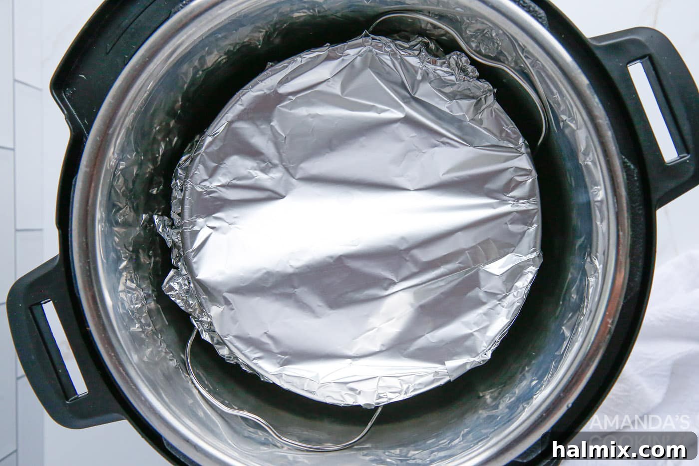 A foil-wrapped cheesecake sits on the trivet inside an Instant Pot, ready for pressure cooking.