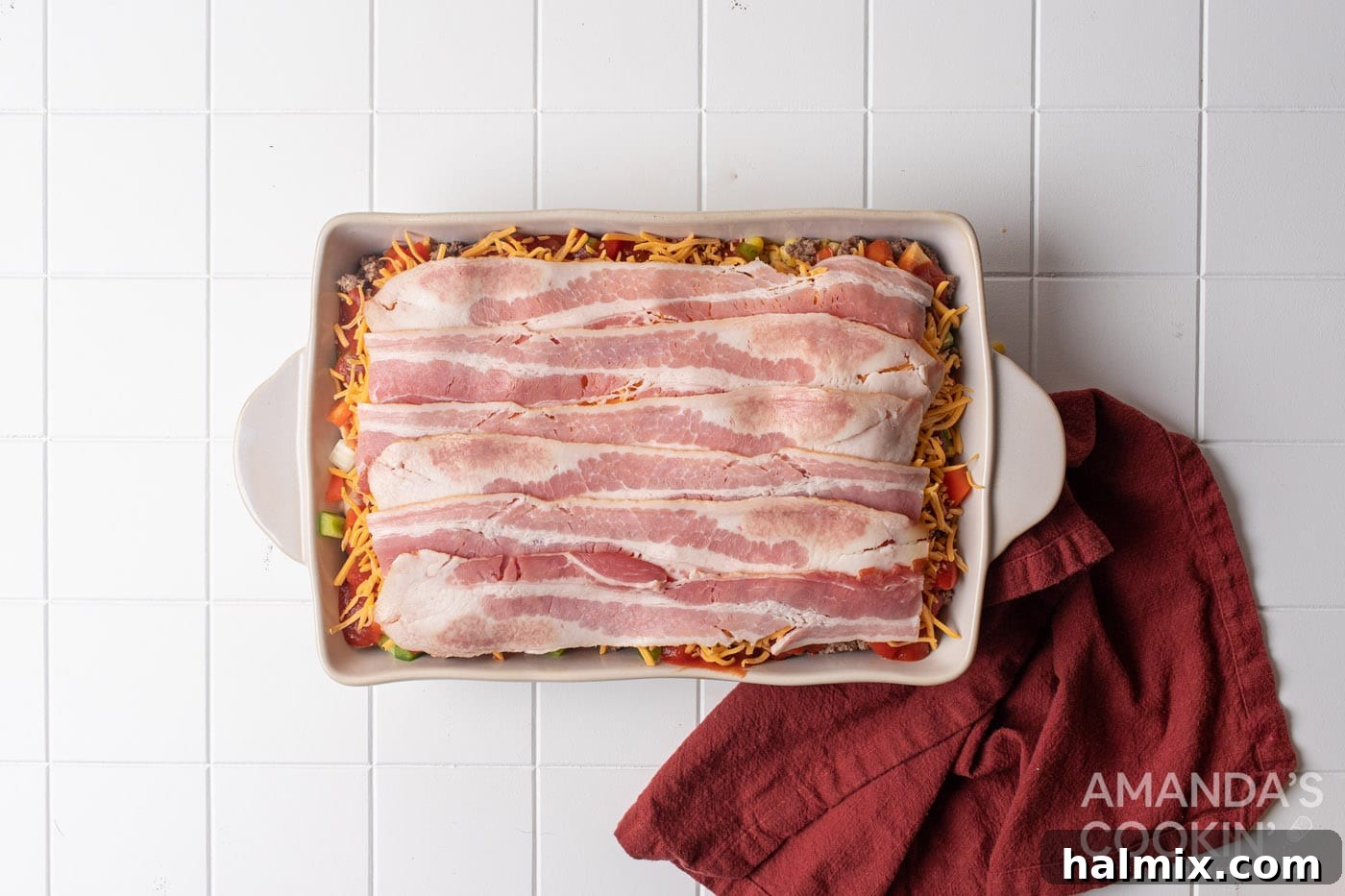 raw bacon strips are laid on top as the final layer of the casserole