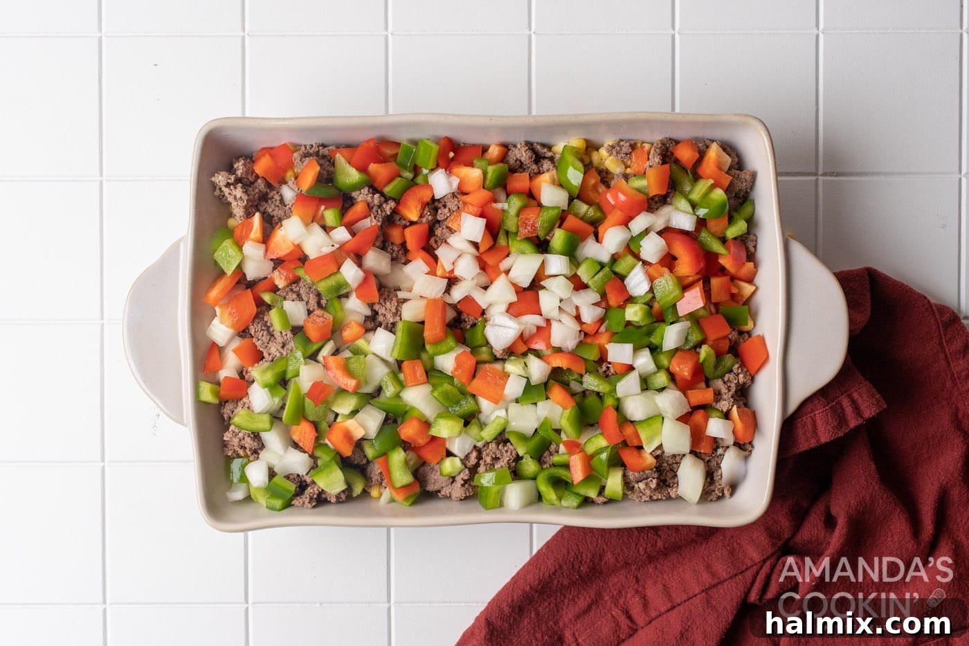 chopped peppers and onion layered on top of ground beef in a baking dish