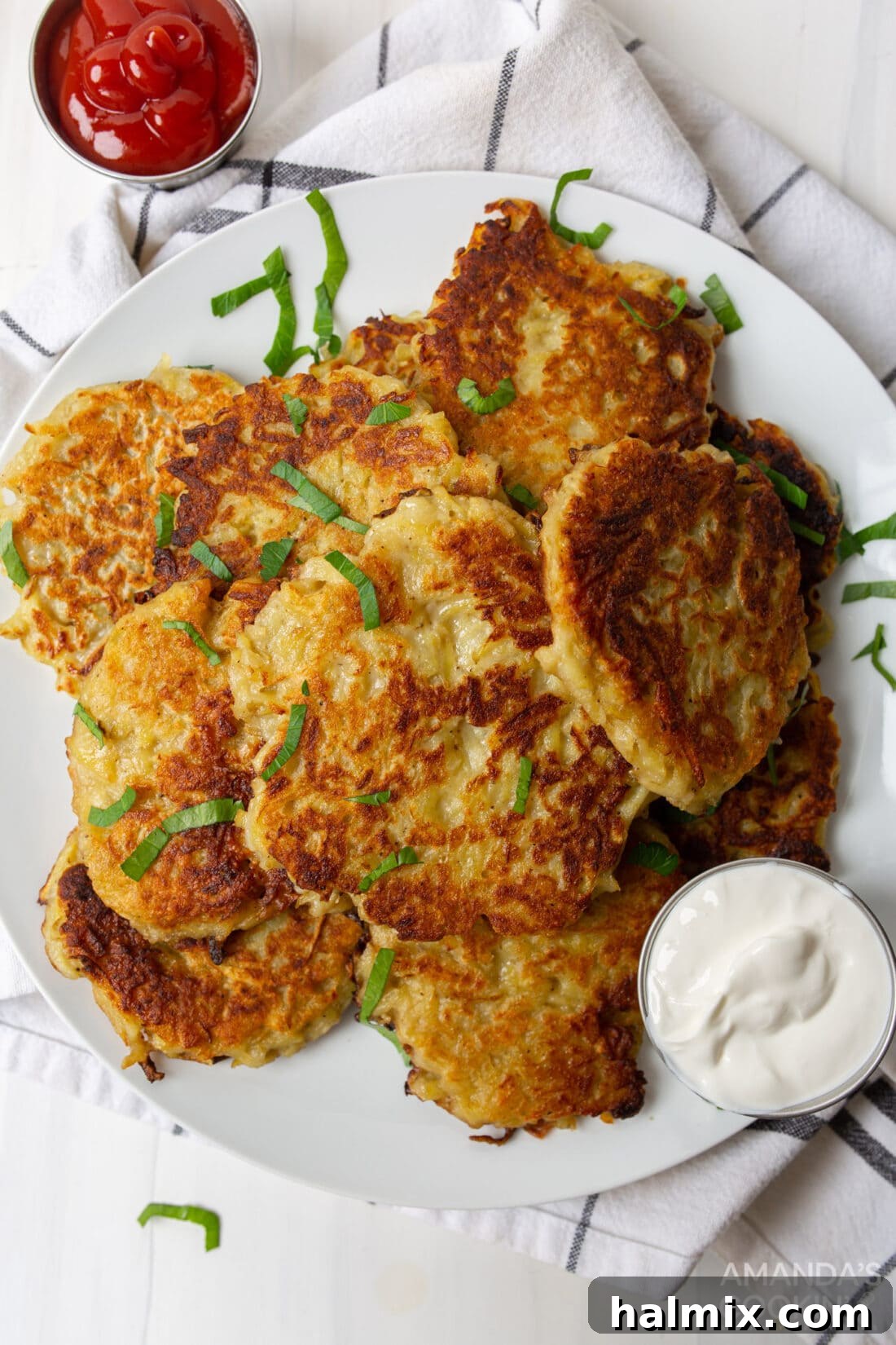 Plate of perfectly fried potato pancakes, garnished with fresh herbs and a side of sour cream