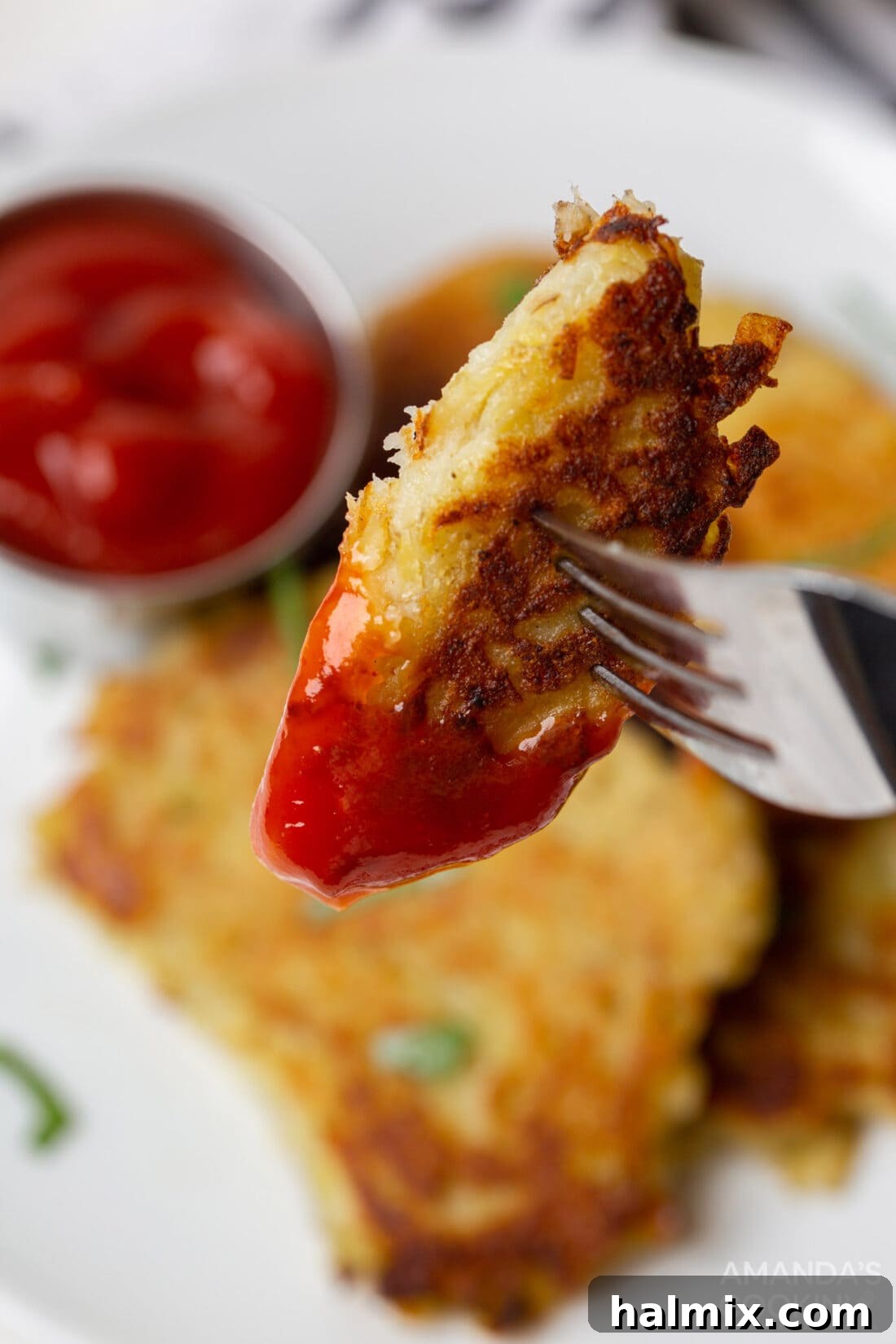 A single crispy potato pancake being dipped into a small bowl of ketchup