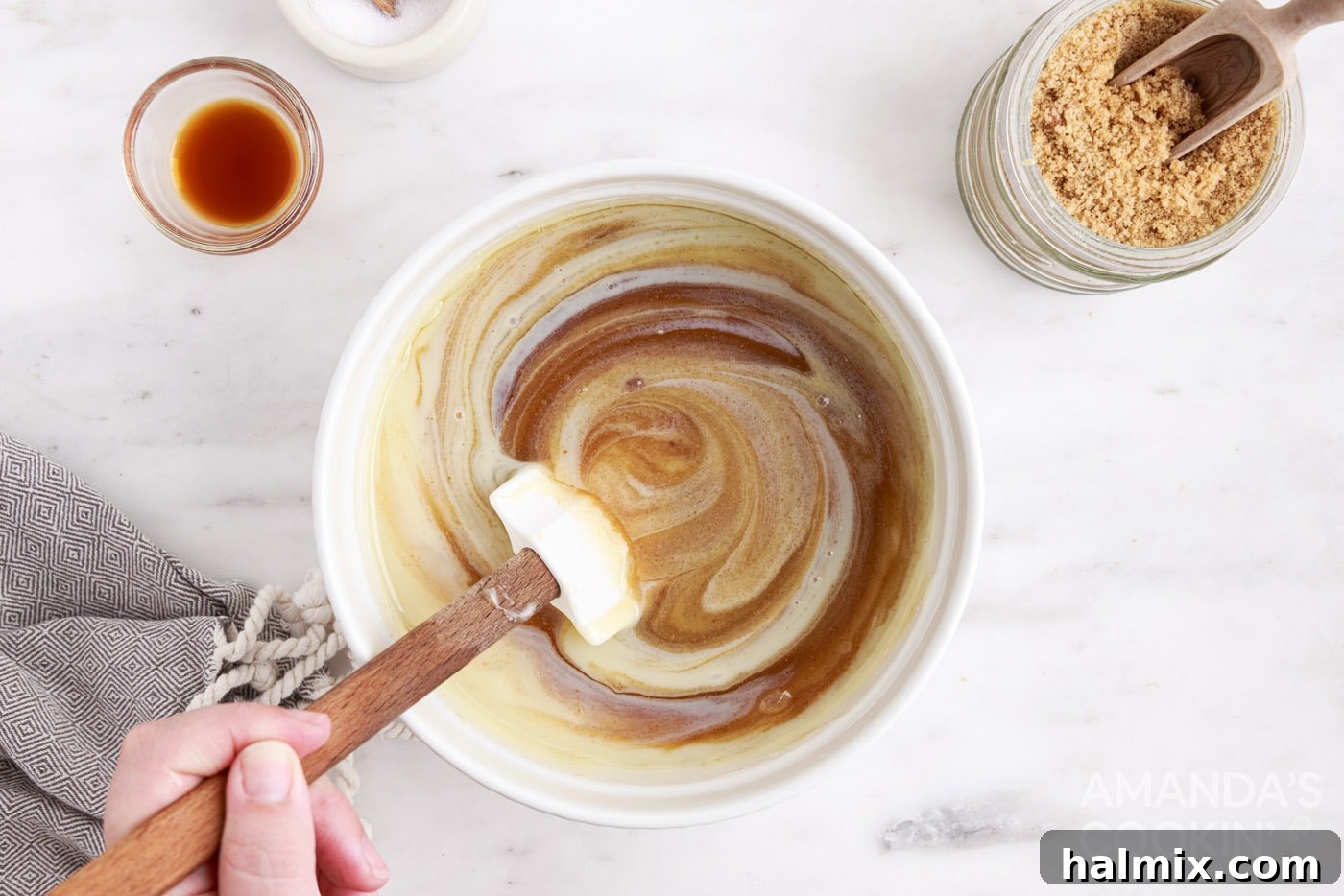 Sweetened condensed milk being whisked into a bowl of boiling sugar mixture for caramels.
