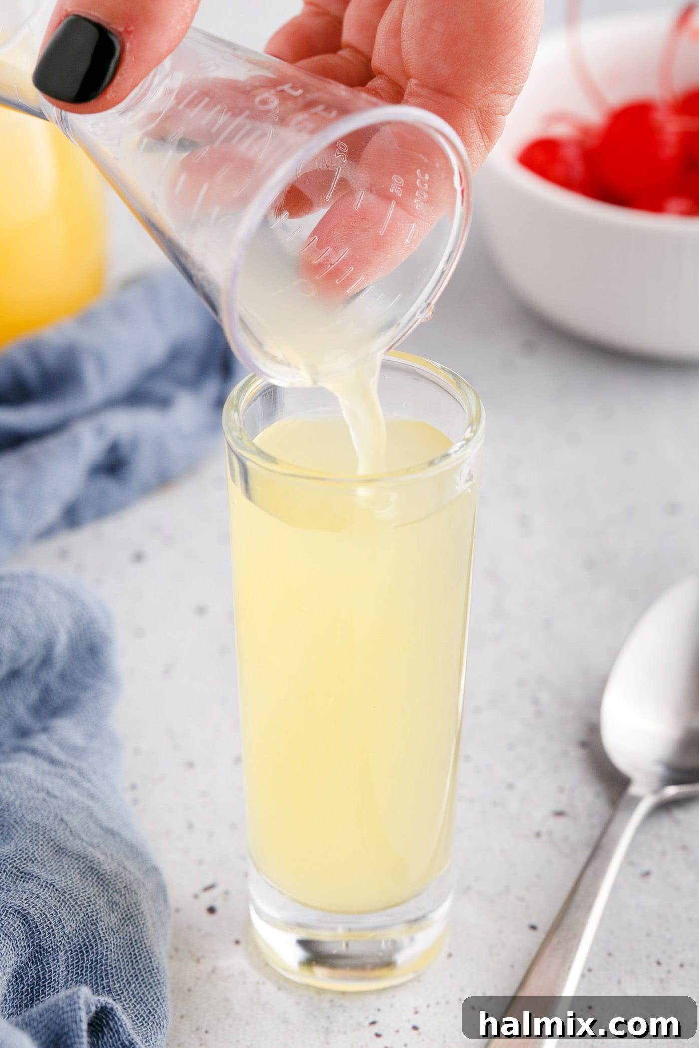 Pouring pineapple juice into a shot glass already containing vanilla vodka.