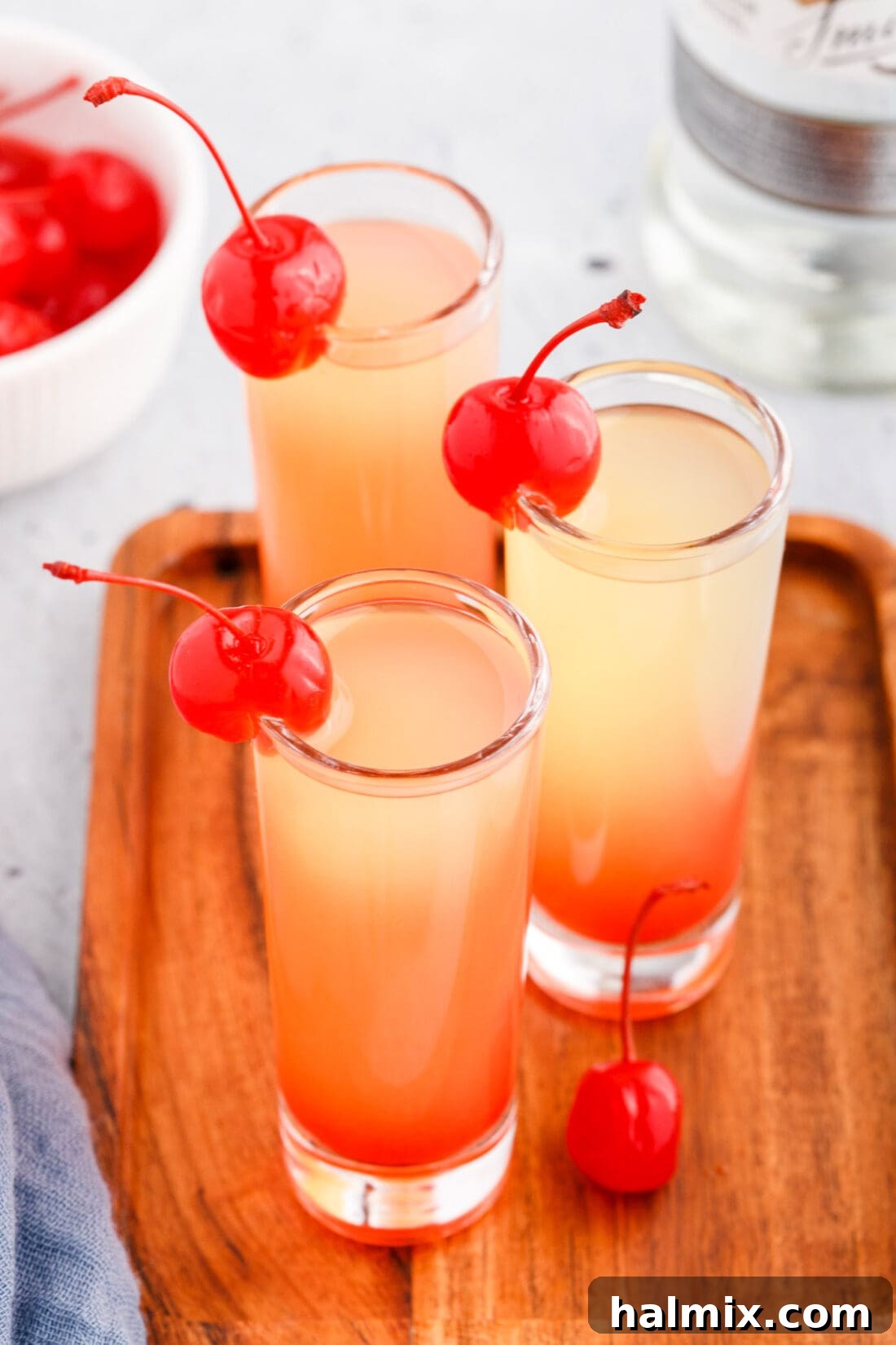 Overhead view of several Pineapple Upside Down Cake Shots with maraschino cherry garnishes.
