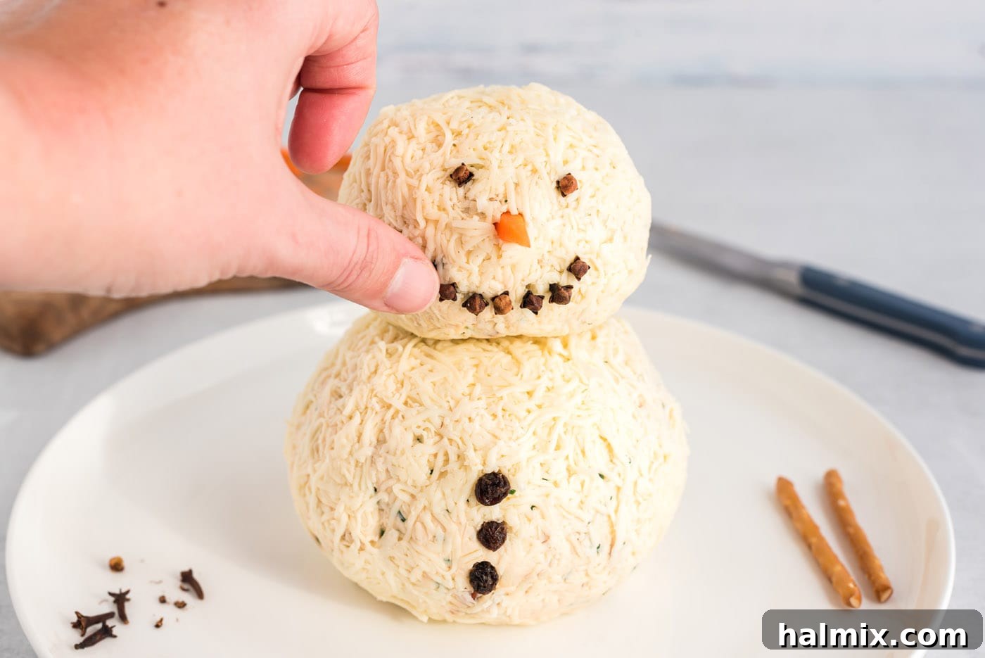 Festive Snowman Cheeseball 11 hand pressing cloves into snowman cheeseball