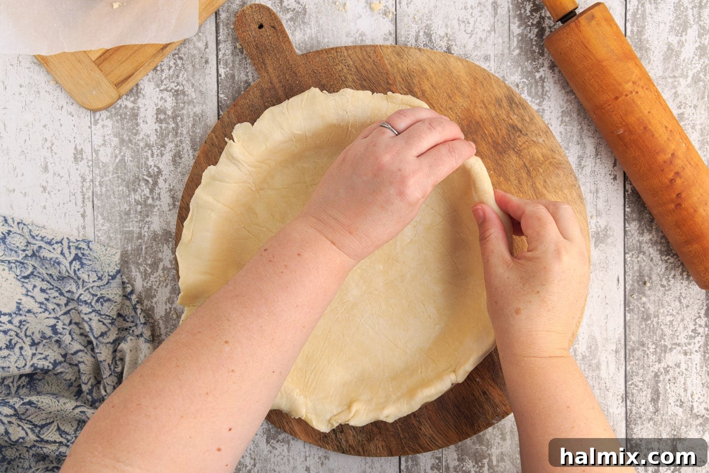Chef's hands folding pie dough under itself to create a thick, reinforced edge