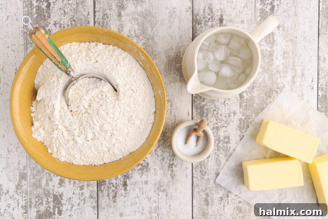 Close-up of butter cubes, flour, salt, and a glass of ice water, essential ingredients for pie crust