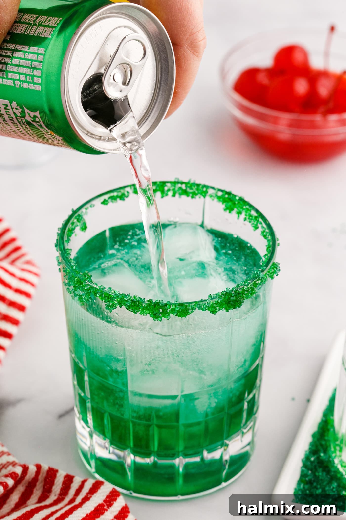 Close-up image of lemon-lime soda being poured into a Grinch Cocktail glass with a sugared rim, completing the drink preparation.