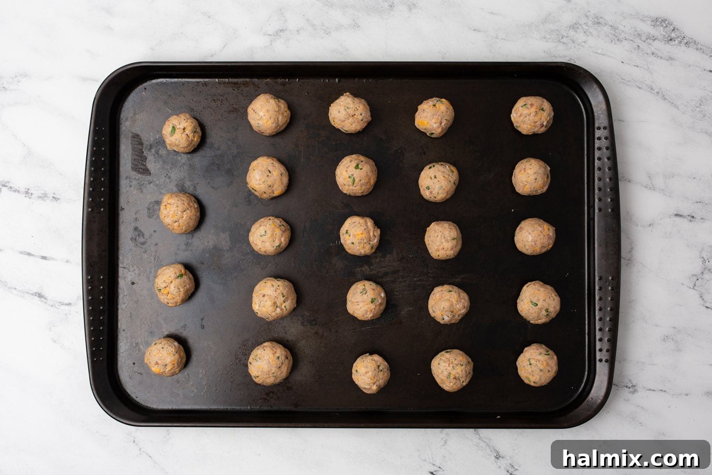 Savory Sausage Bites 7 Uncooked sausage balls perfectly arranged in neat rows on a baking sheet, ready for the oven.