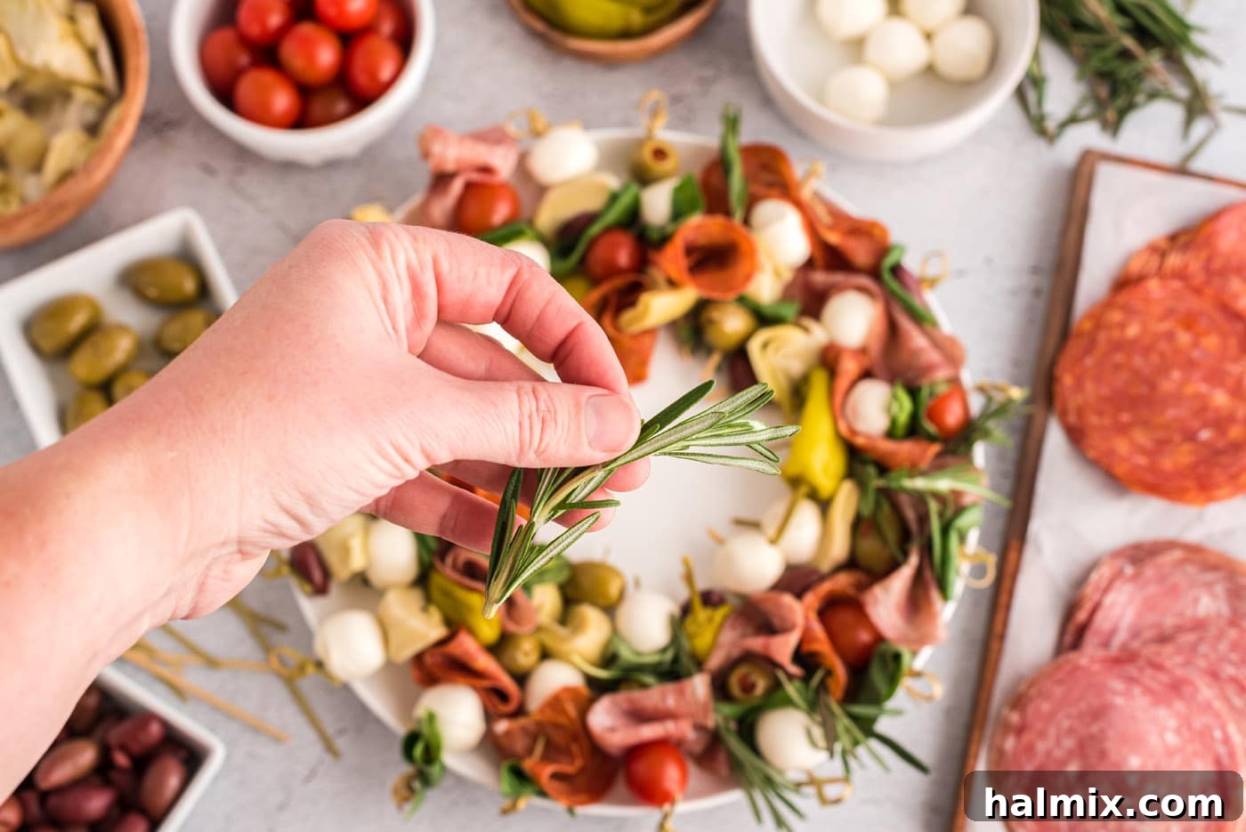 Hand placing a rosemary sprig over the antipasto wreath