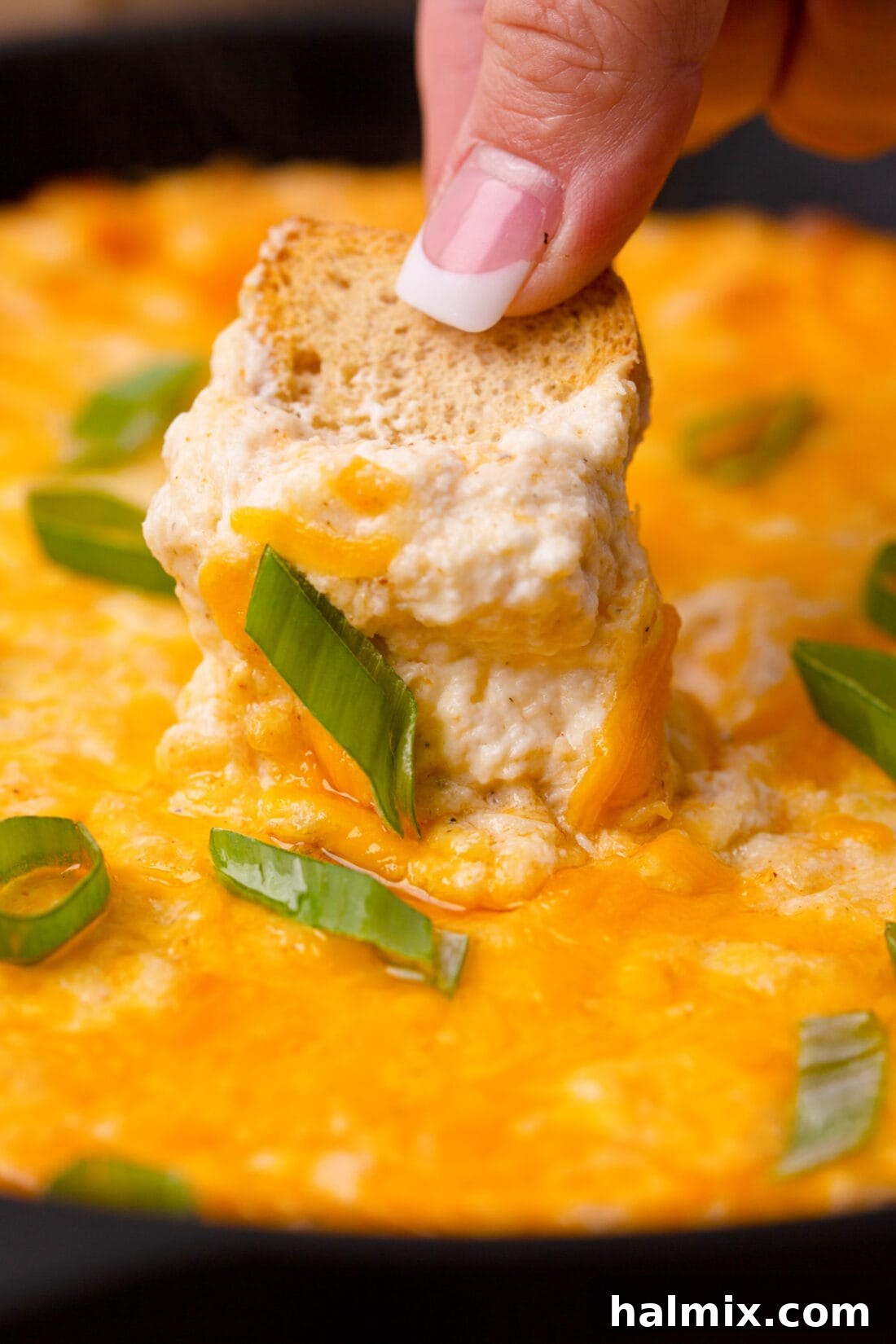 A serving spoon scooping creamy Crab Dip from a hot skillet, ready to be enjoyed.