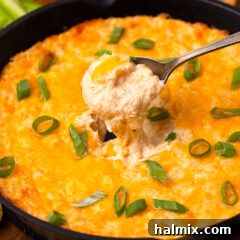 Delicious Crab Dip in a skillet with a spoon, garnished with green onions.