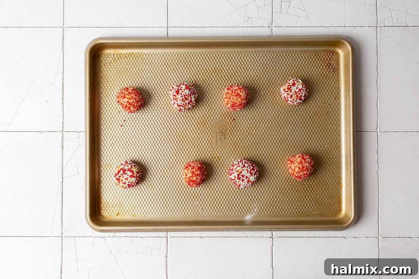 Peanut butter cookie dough balls being rolled in a bowl of colorful festive sprinkles