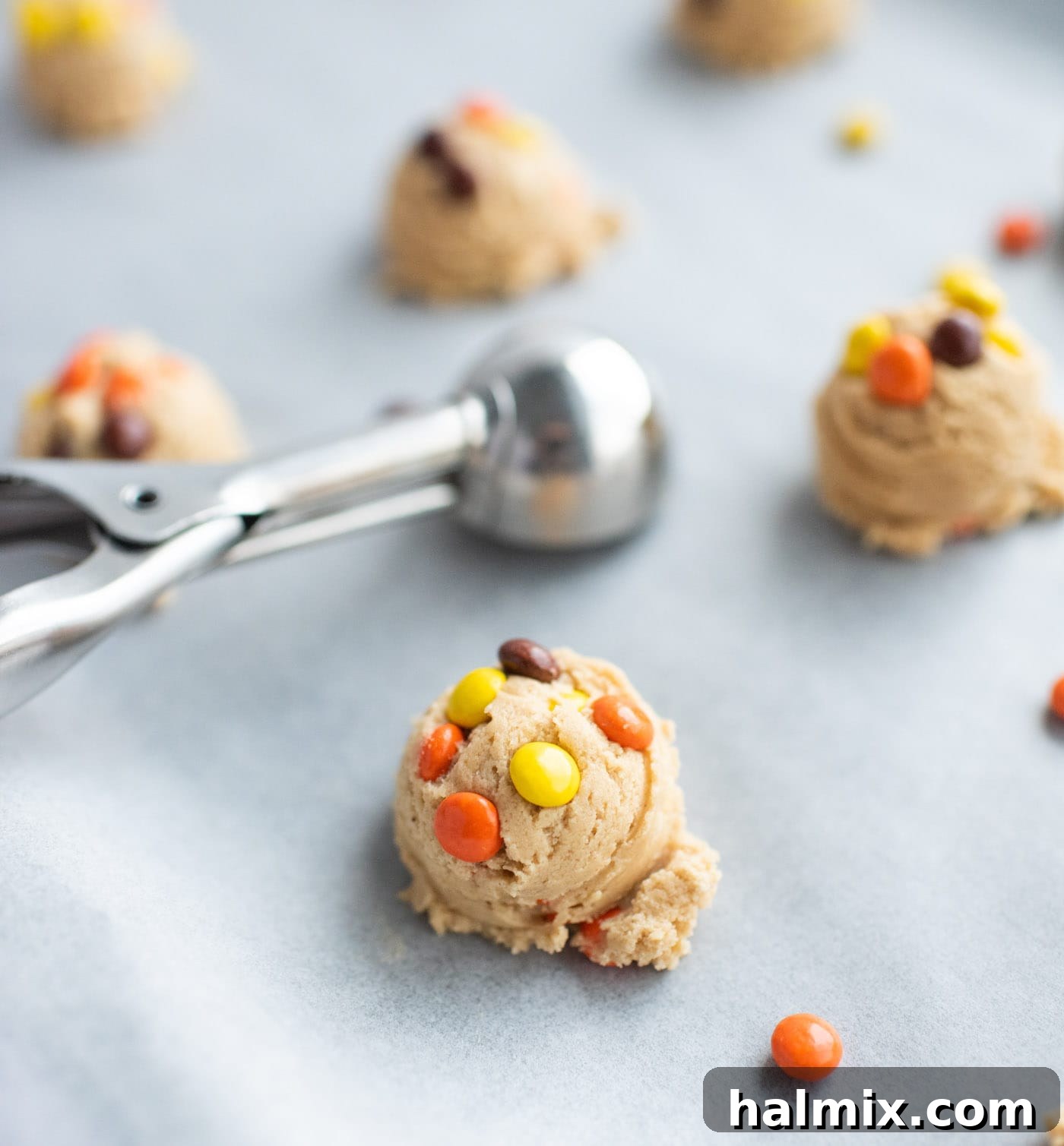 Cookie scoop adding dough balls to parchment paper lined baking sheet
