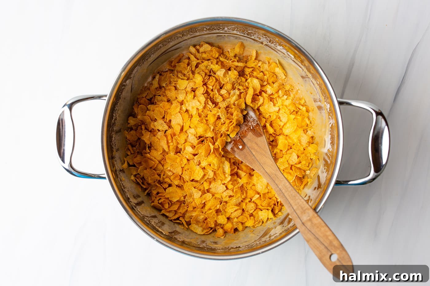 wooden spoon stirring cornflakes into marshmallows