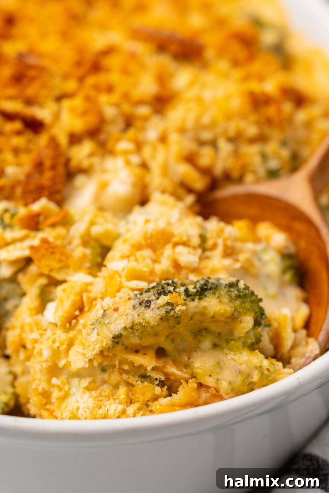 Wooden spoon serving a portion of rich and creamy Cheesy Broccoli Casserole from a baking dish.
