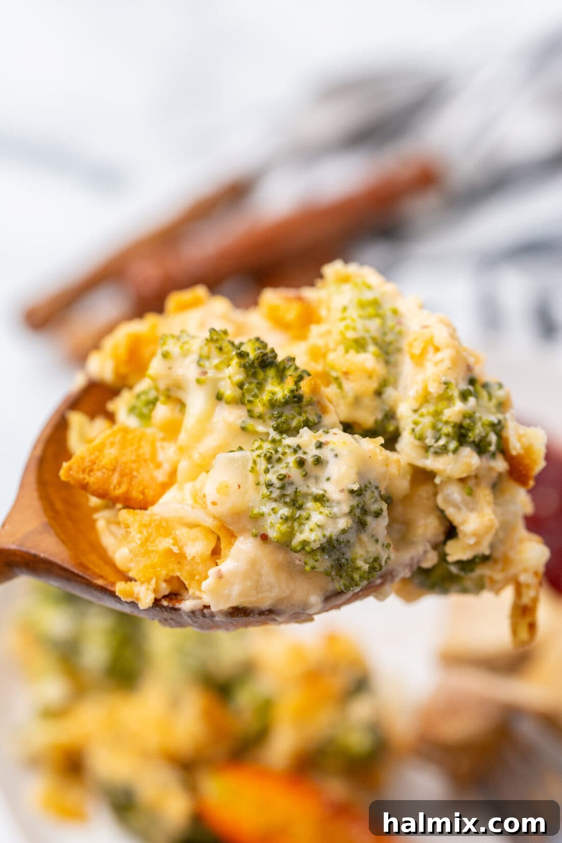 A wooden spoon scooping out a generous portion of hot, cheesy broccoli casserole.