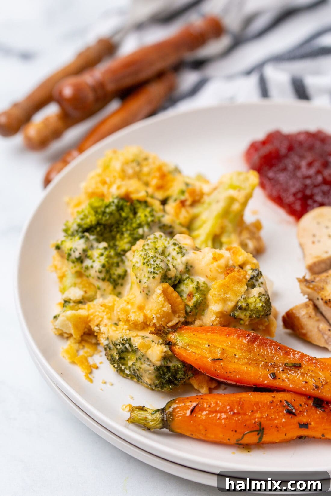A serving of Cheesy Broccoli Casserole on a white plate, accompanied by a full dinner spread.