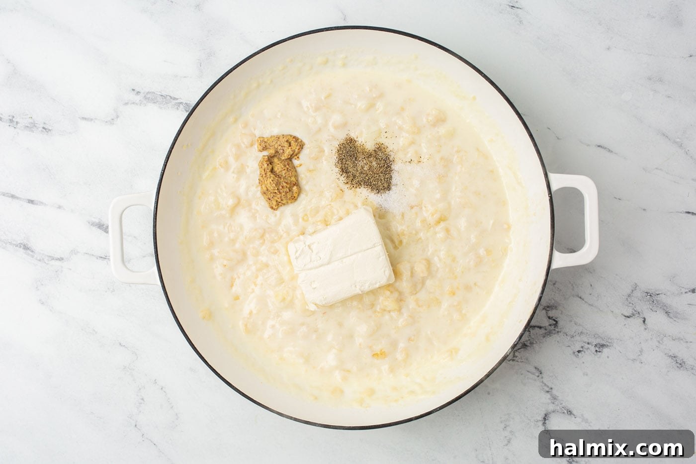 Cream cheese and Dijon mustard being stirred into a rich butter and flour roux.