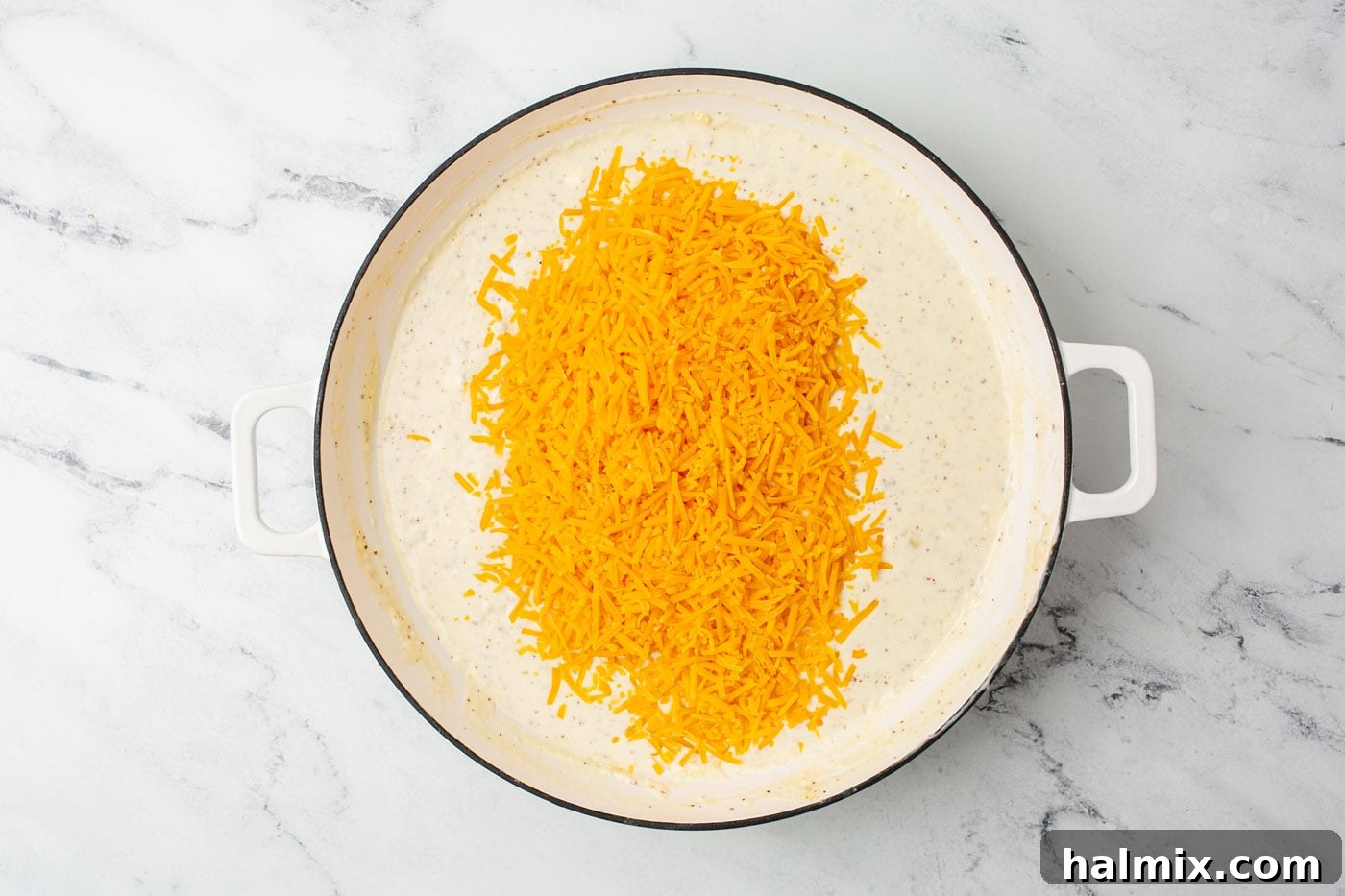 Melted cheddar cheese being stirred into a creamy sauce in a skillet.
