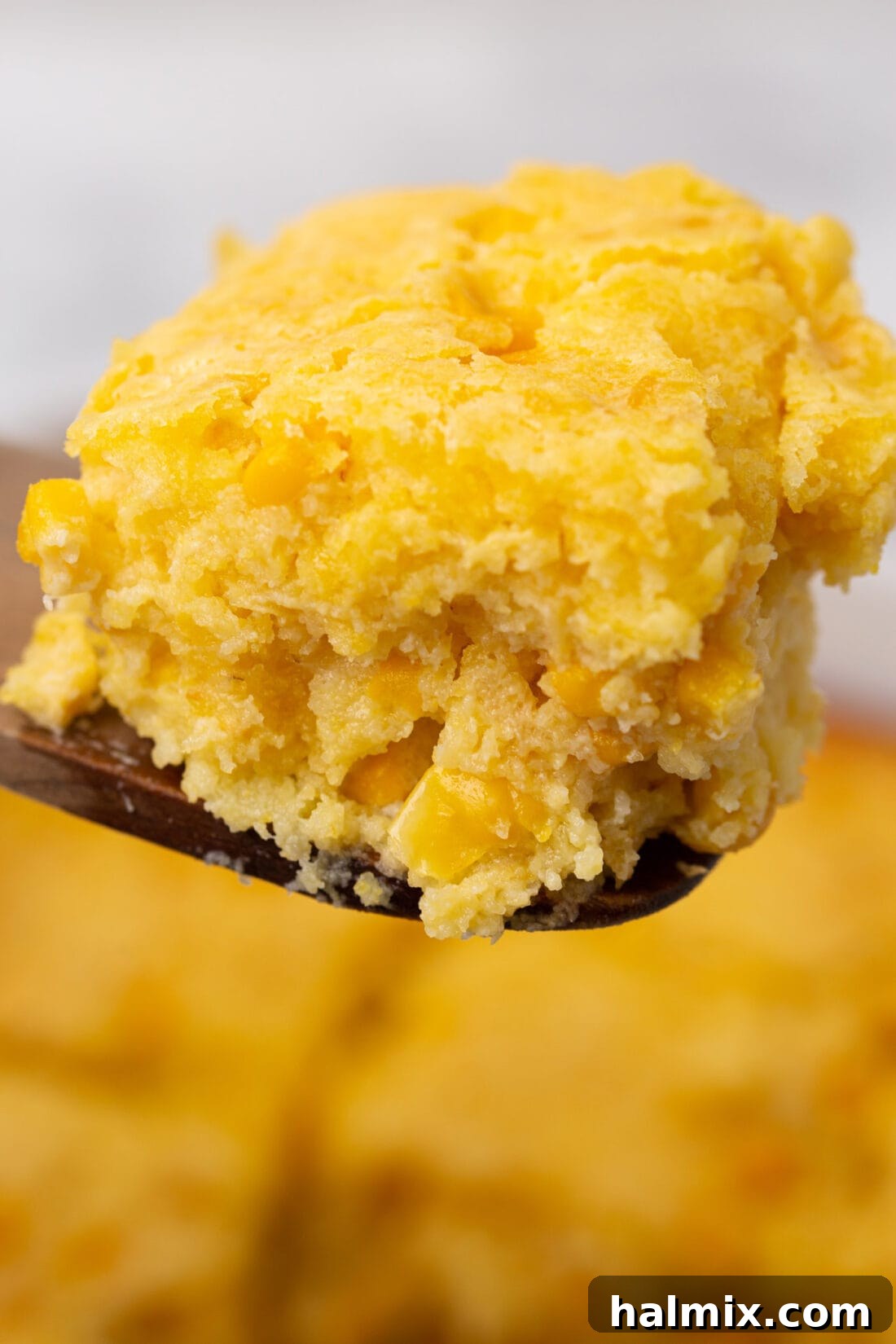 A spoonful of fluffy corn casserole being lifted from the baking dish, showing its creamy texture.