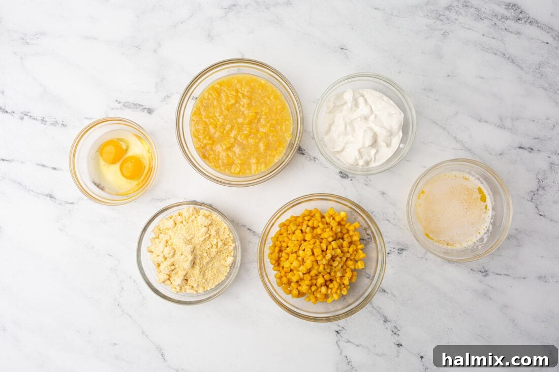 Arrangement of fresh ingredients including cornbread mix, canned corn, sour cream, butter, and eggs, laid out for making corn casserole.