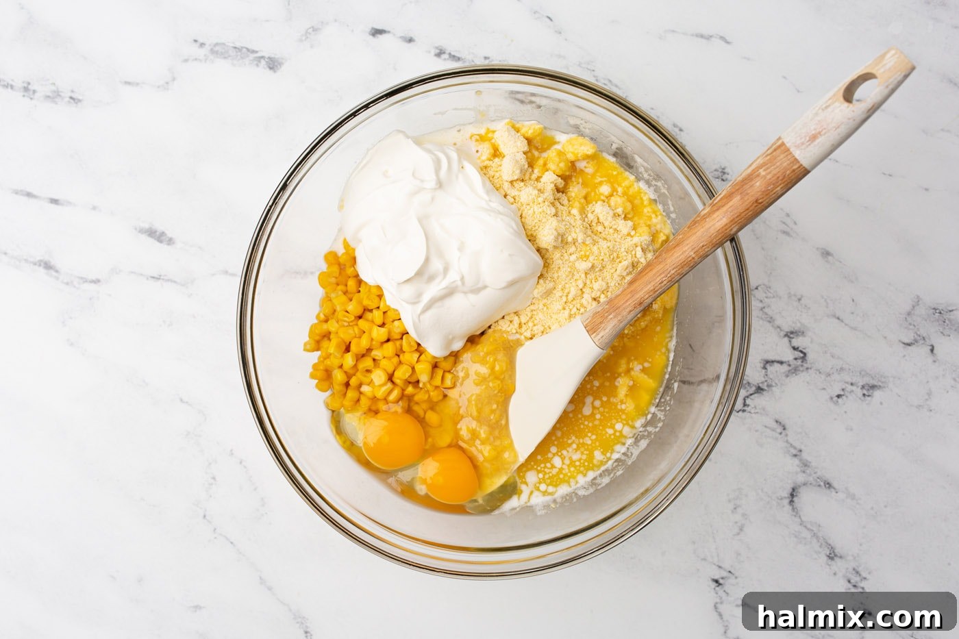 All corn casserole ingredients being mixed together in a large white bowl with a spatula.