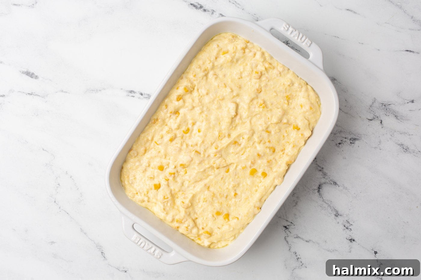 The mixed corn casserole ingredients poured into a glass baking dish, ready for the oven.