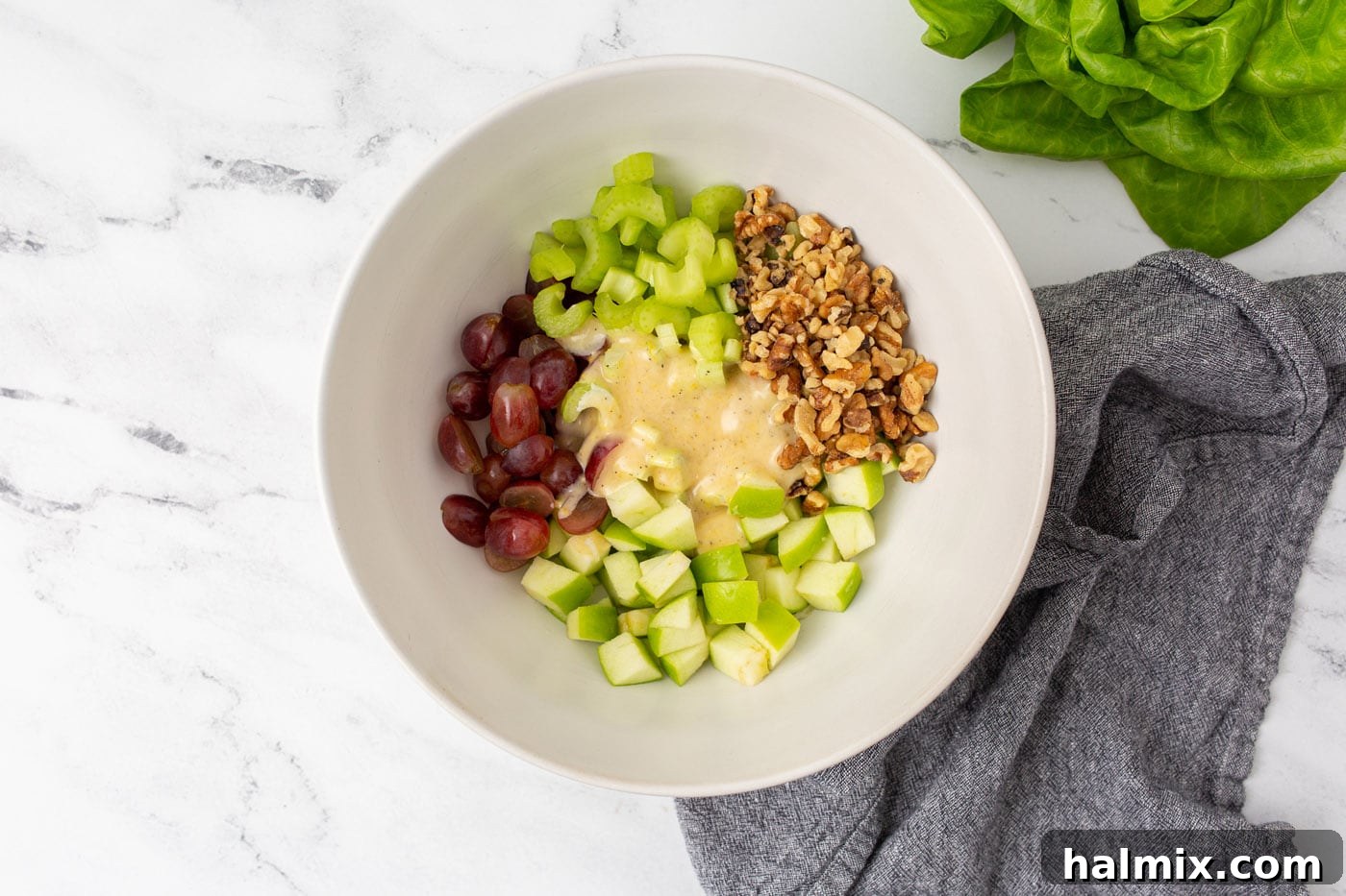 Waldorf salad with the creamy dressing poured over and being tossed in a bowl.