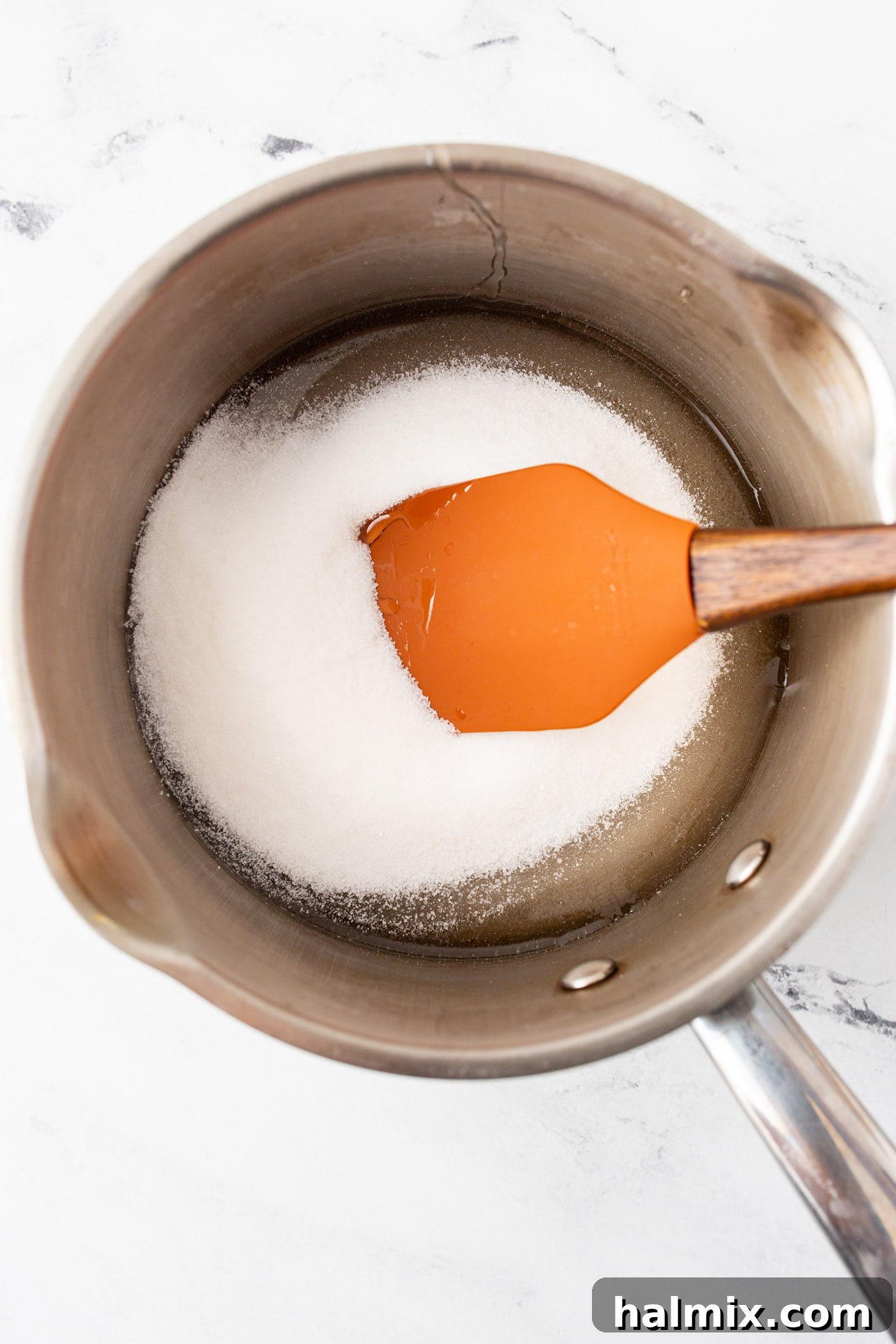 Corn syrup and sugar being stirred with a rubber spatula in a stainless steel pot