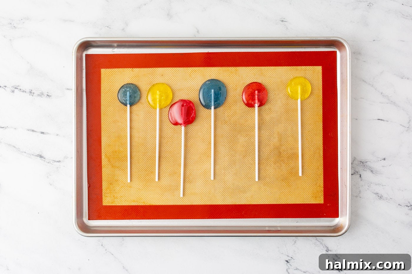 Freshly poured homemade lollipops on a silicone baking sheet with sticks inserted