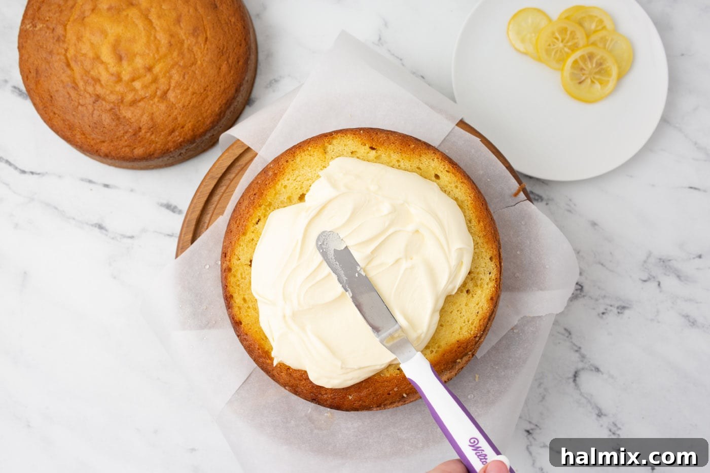 An icing spatula spreading smooth lemon buttercream frosting onto a cake layer.