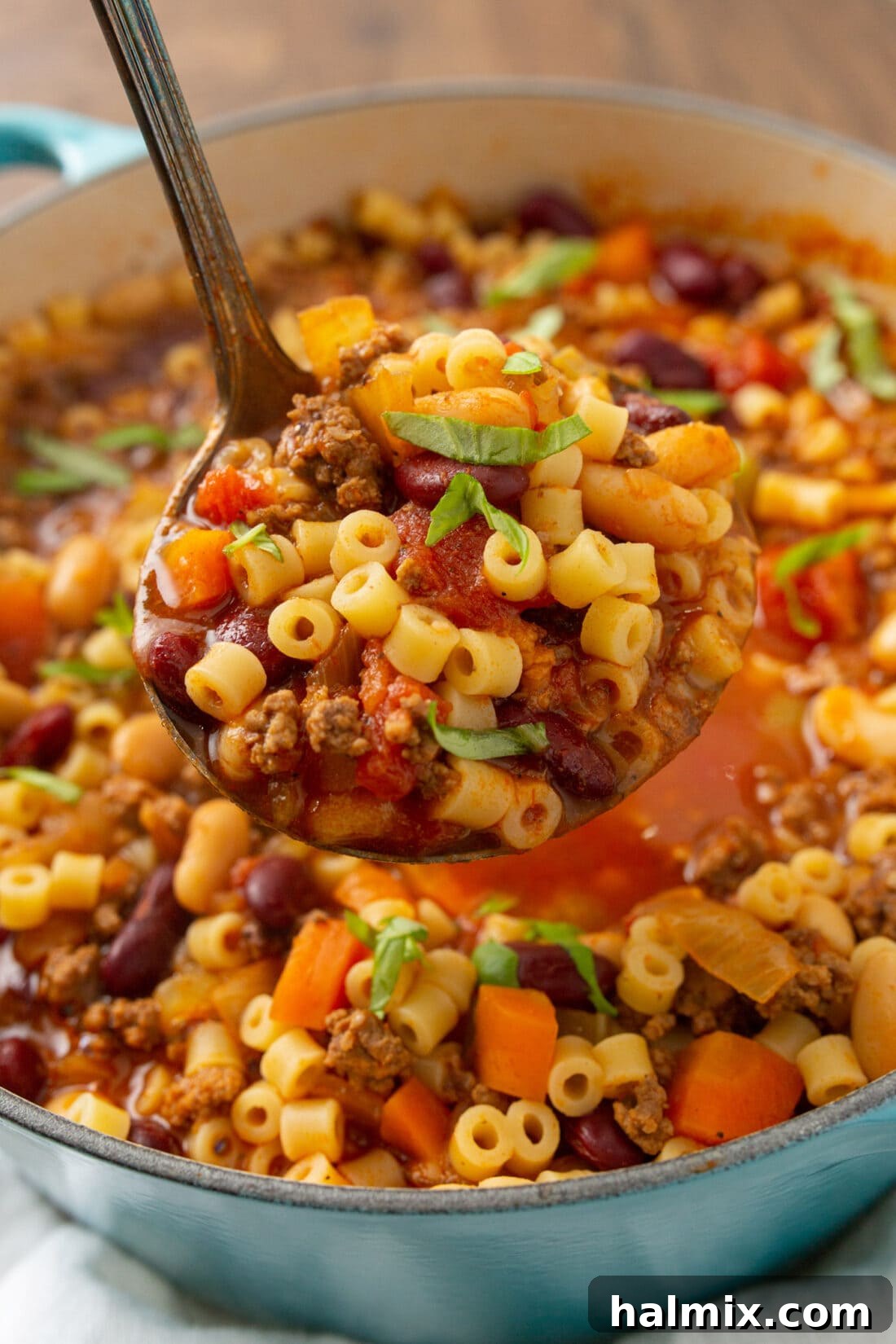 A chef ladling out a generous portion of Pasta Fagioli soup into a serving bowl.