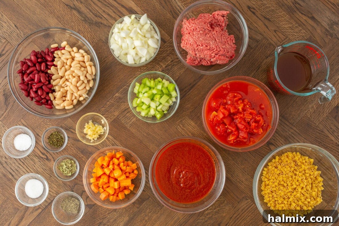 An array of fresh ingredients laid out for making Pasta Fagioli, including vegetables, ground beef, pasta, and canned goods.