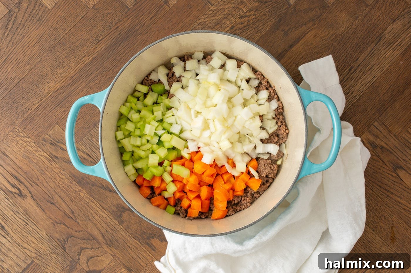 Diced carrots, celery, and onion being sautéed with browned ground beef in a large soup pot, releasing rich aromas.