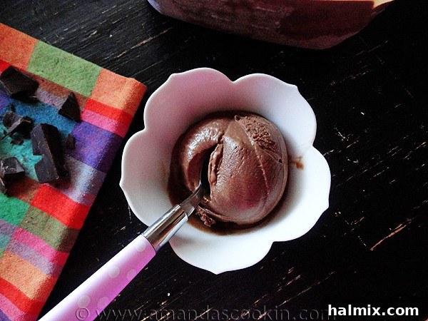 A scoop of Black Cow Ice Cream in an elegant white bowl, accompanied by a small silver spoon ready for a taste.