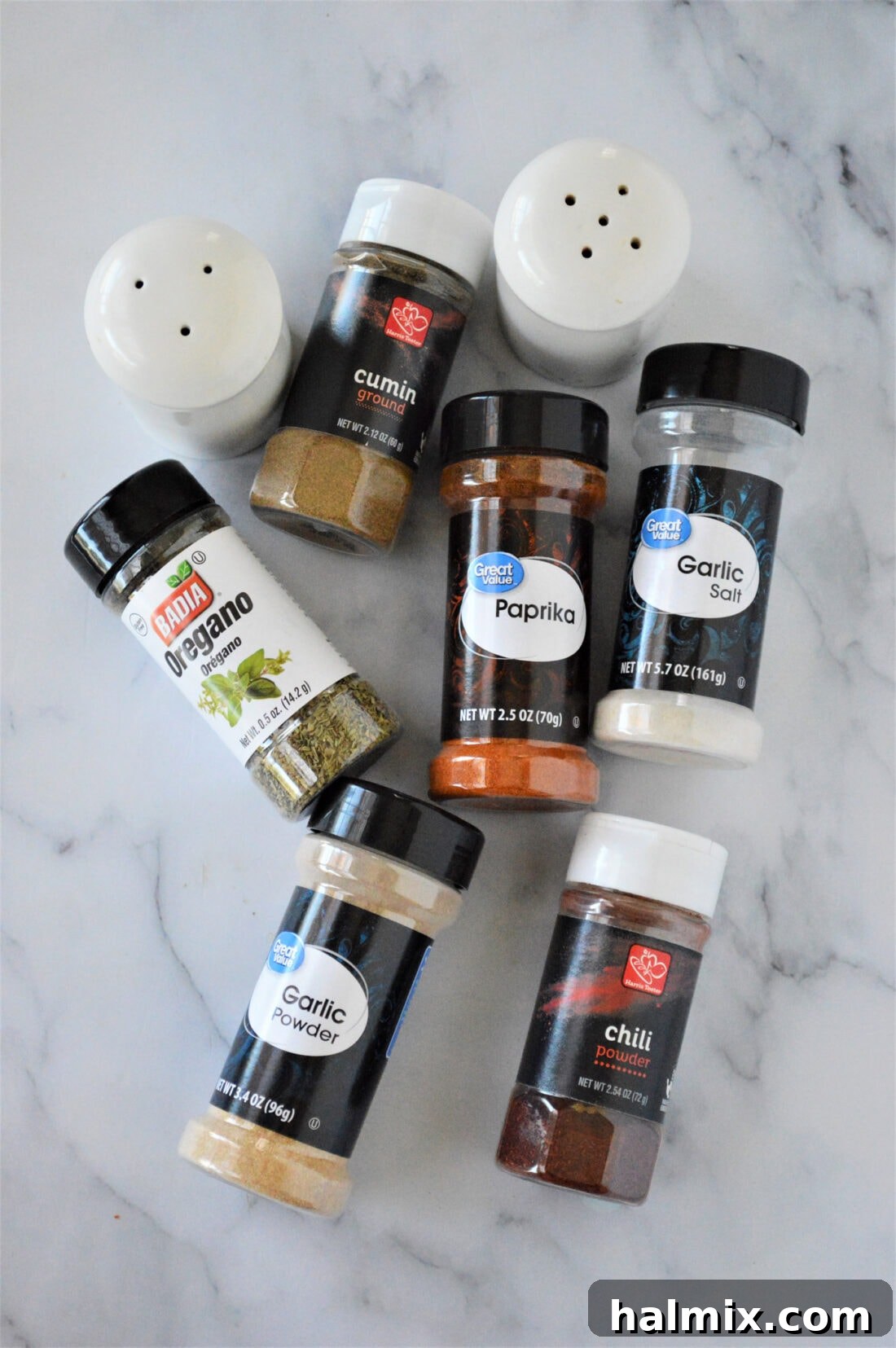 Individual ingredients for French Fry Seasoning laid out on a clean surface, including jars of garlic salt, cumin, oregano, chili powder, garlic powder, paprika, salt, and pepper.