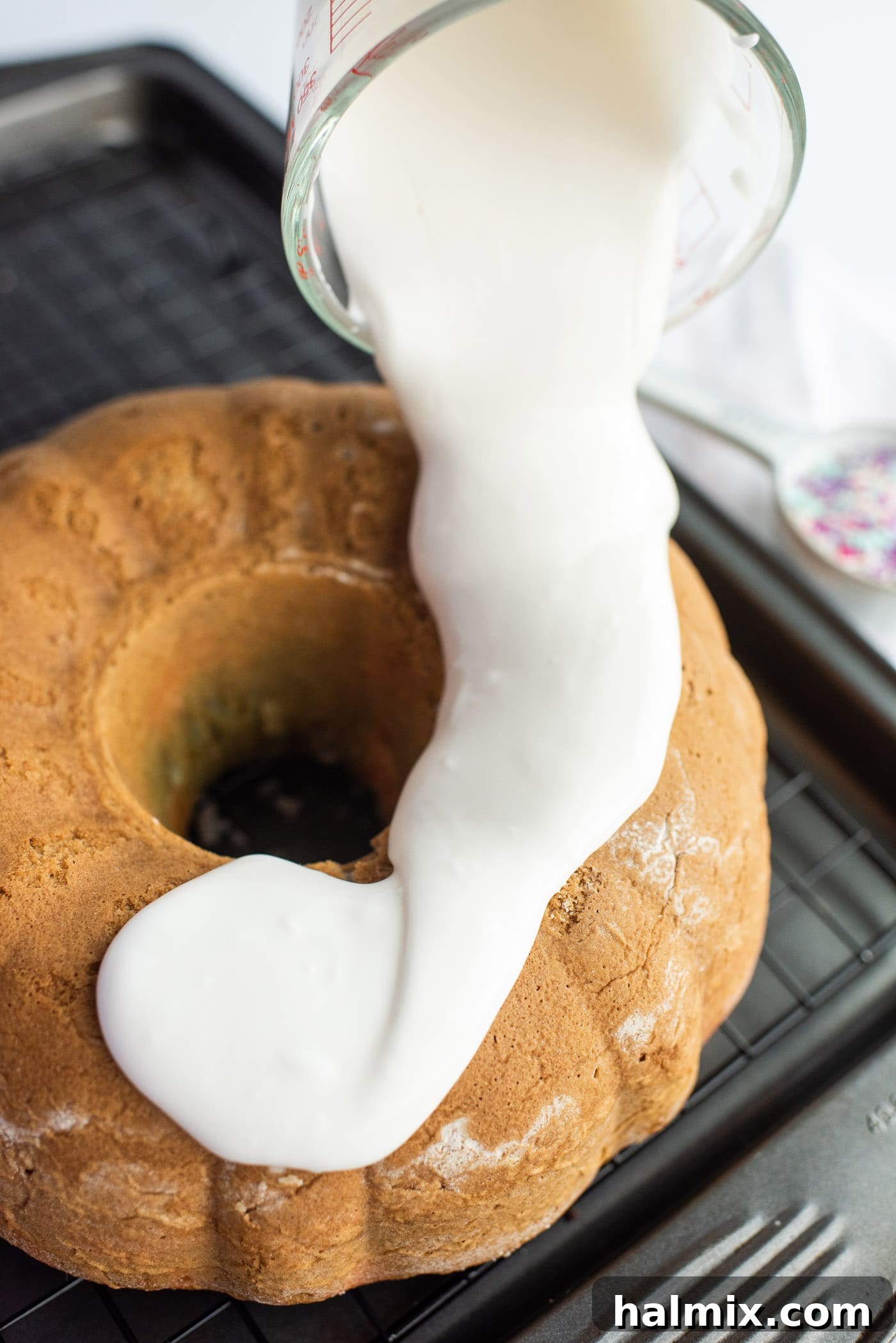 Pouring smooth vanilla glaze over the cooled Unicorn Bundt Cake, creating beautiful drips.
